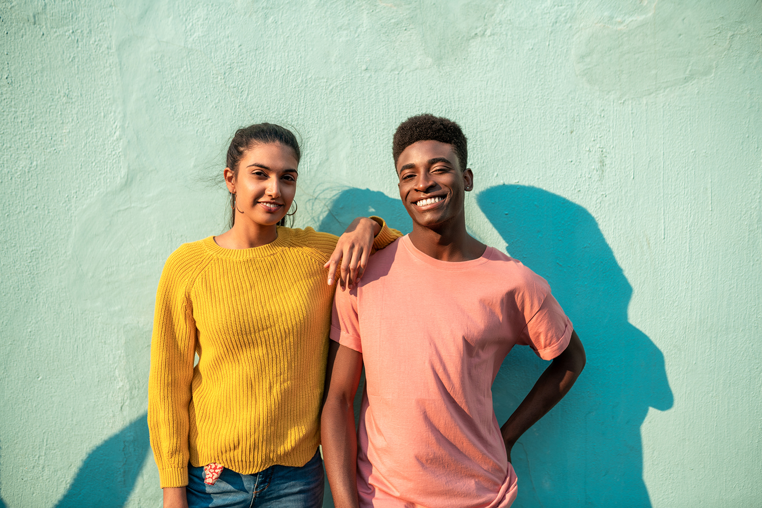 2 young teenagers smiling against a blue wall